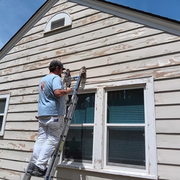 Painter preparing siding from a ladder